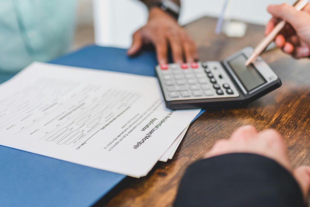 Hands using a calculator with real estate documents on a desk, indicating a financial transaction or meeting.